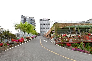 A street with buildings, a road with a yellow line, and flower beds on the sides. - Oceanview Resortel (Boryeong)