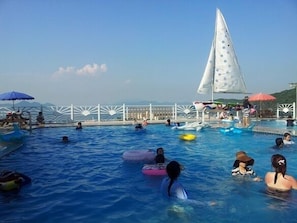 A swimming pool with multiple people, some on inflatable rings, and a sailboat in the background. - Oceanview Resortel (Boryeong)
