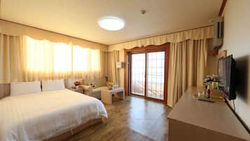 A hotel room with a large bed, a desk, a chair, a television, and a sliding glass door to the outside.