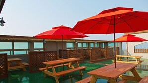 An outdoor patio area with wooden picnic tables and red umbrellas.