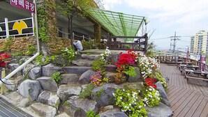 A stone staircase with colorful flowers, a wooden deck with benches, and a building with a green roof.