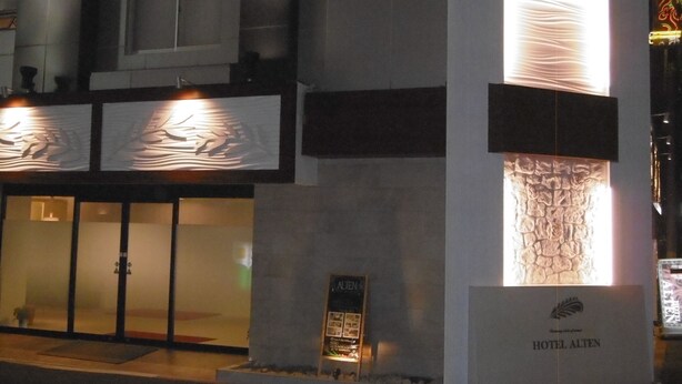 A modern hotel facade with a prominent illuminated sign, a stone-textured wall feature, and a clear entrance with glass doors. - Hotel Alten (Osaka)