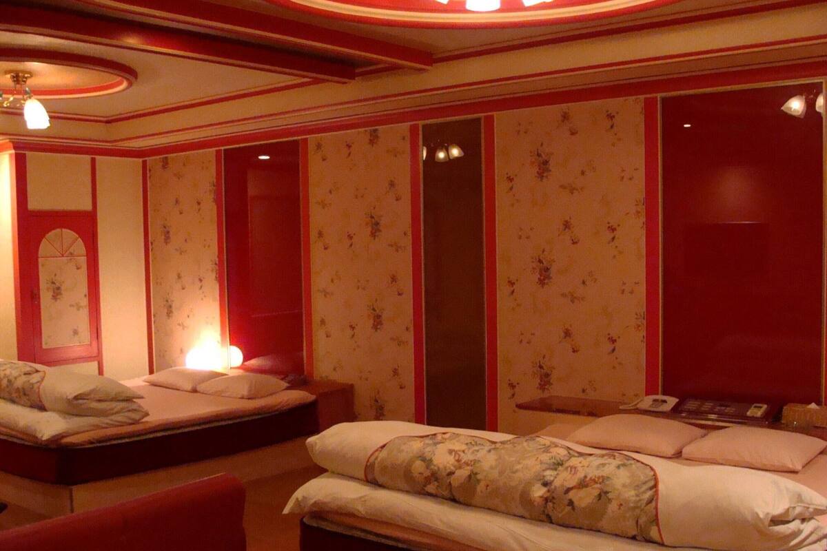 A hotel room with two beds, floral wallpaper, a red accent wall, and a ceiling light fixture.