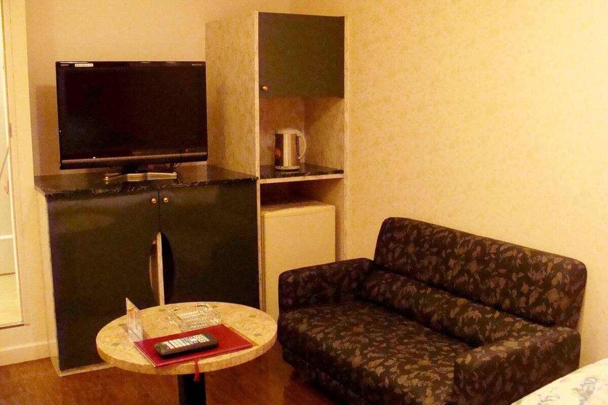A compact living space with a sofa, a small table with a remote control, a television, a cabinet, and a coffee maker.