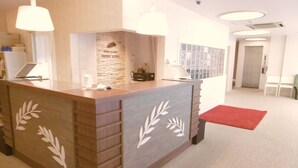 A hotel reception area with a wooden reception desk, two pendant lights, a red carpet, and a stone wall with a logo. - Hotel Alten (Osaka)