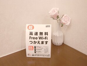A sign with Japanese text and a USEN logo, placed on a table next to a white vase with pink roses. - Hotel Alten (Osaka)