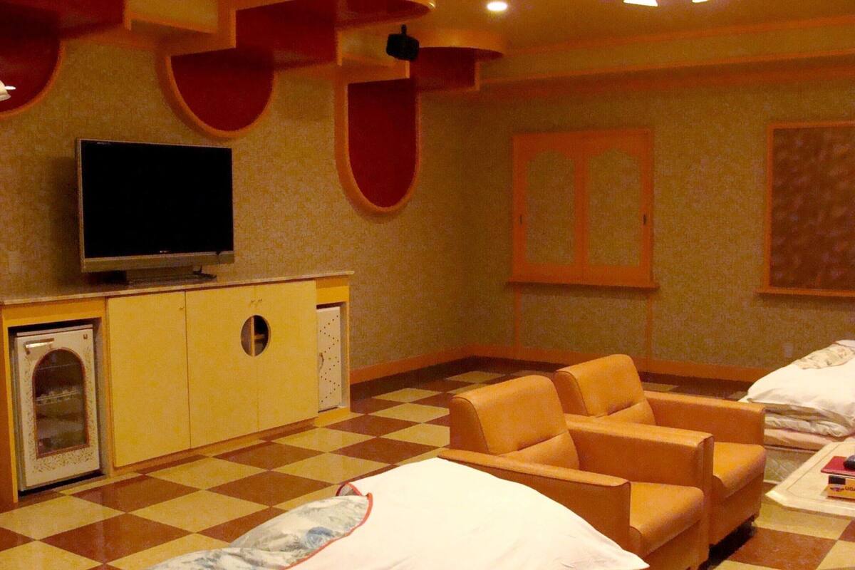 A hotel room with a checkered floor, a bed, a sofa, a television, and a minibar.