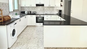Uma cozinha moderna com armários brancos, máquina de lavar embutida, micro-ondas, cafeteira e uma ilha grande com bancada preta.