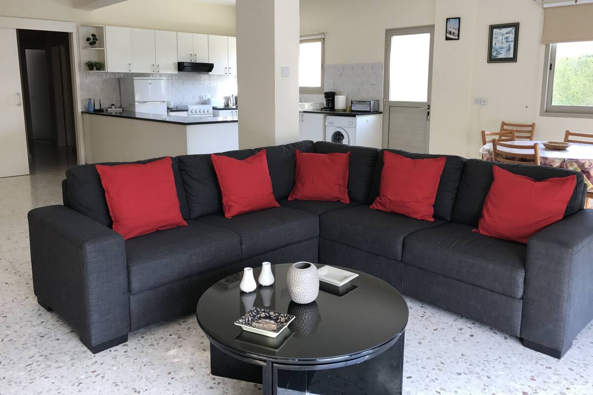 Ein modernes Wohnzimmer mit einer Eckcouch, einem runden Couchtisch und einer Küche im Hintergrund.