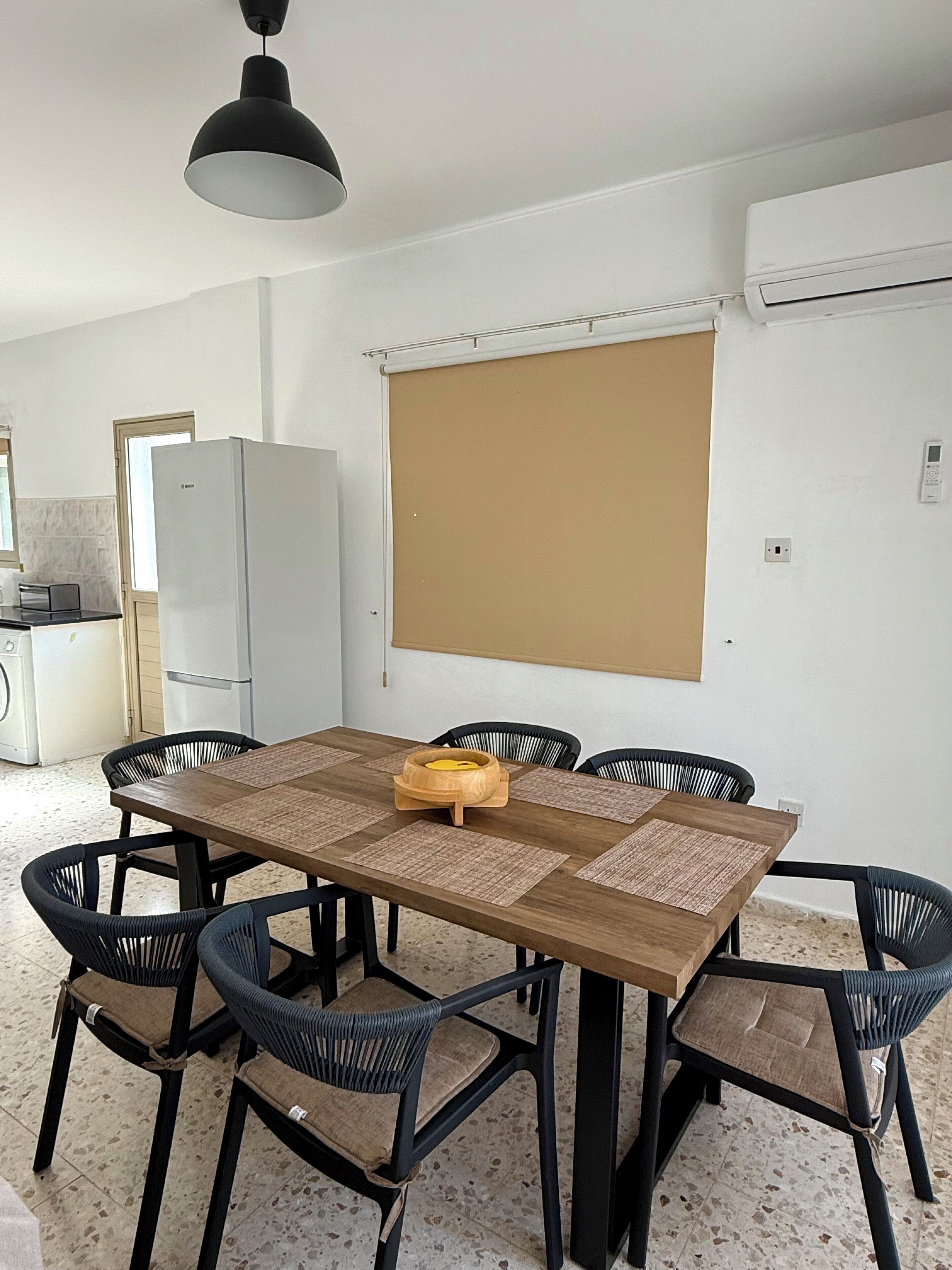 Un espace repas avec une table en bois, des chaises noires et un luminaire au plafond.