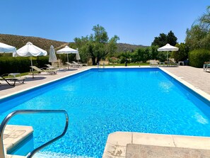 Ein rechteckiger Swimmingpool mit klarem, blauem Wasser, umgeben von Liegestühlen und Sonnenschirmen.