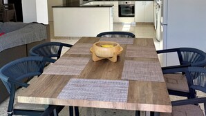 Uma cozinha moderna com armários brancos, uma ilha central e um espaço de jantar com mesa de madeira e cadeiras azuis.