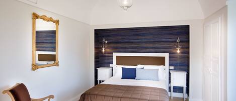 A bedroom with a large bed, a nightstand, a chair, a mirror, and a chandelier.