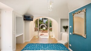 Une chambre à coucher avec un lit, un téléviseur fixé au mur, un miroir et une porte en arc donnant sur un patio.