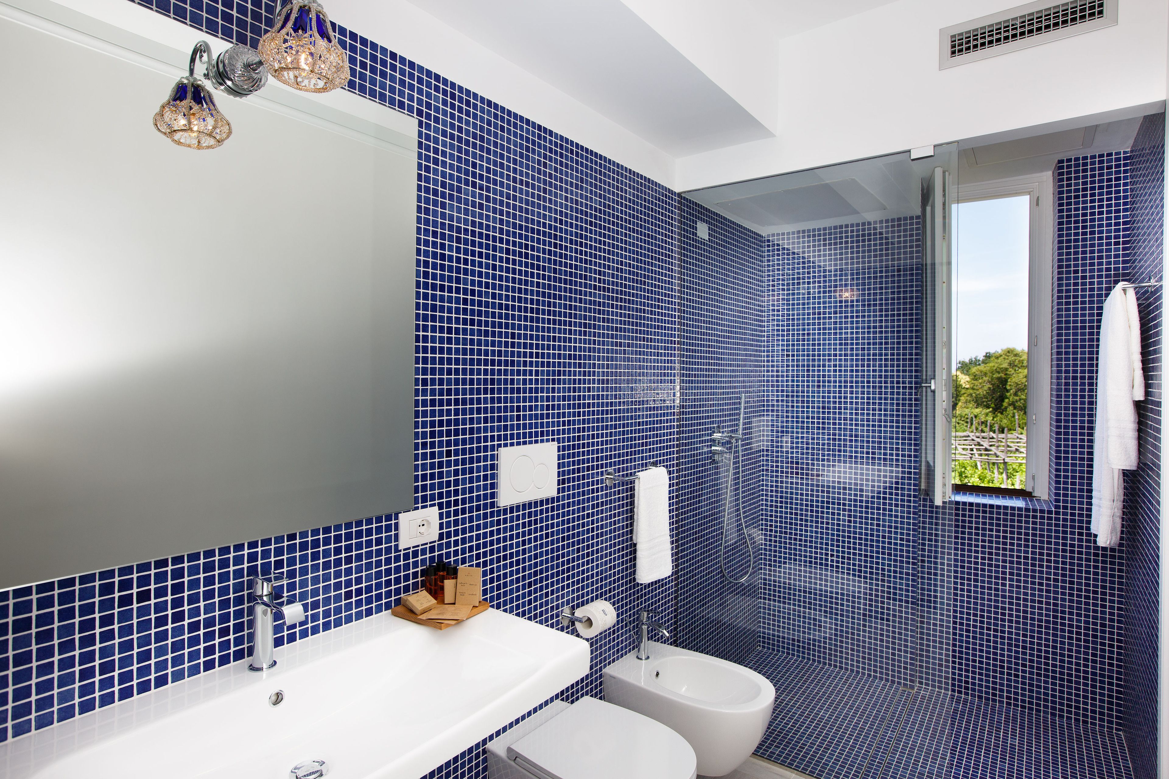 A bathroom with blue mosaic tiles, a white sink, a bidet, and a shower.