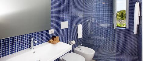 A bathroom with blue mosaic tiles, a white sink, a bidet, and a shower.