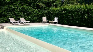 Une piscine aux eaux cristallines, bordée de chaises longues blanches et d’un muret en pierres.