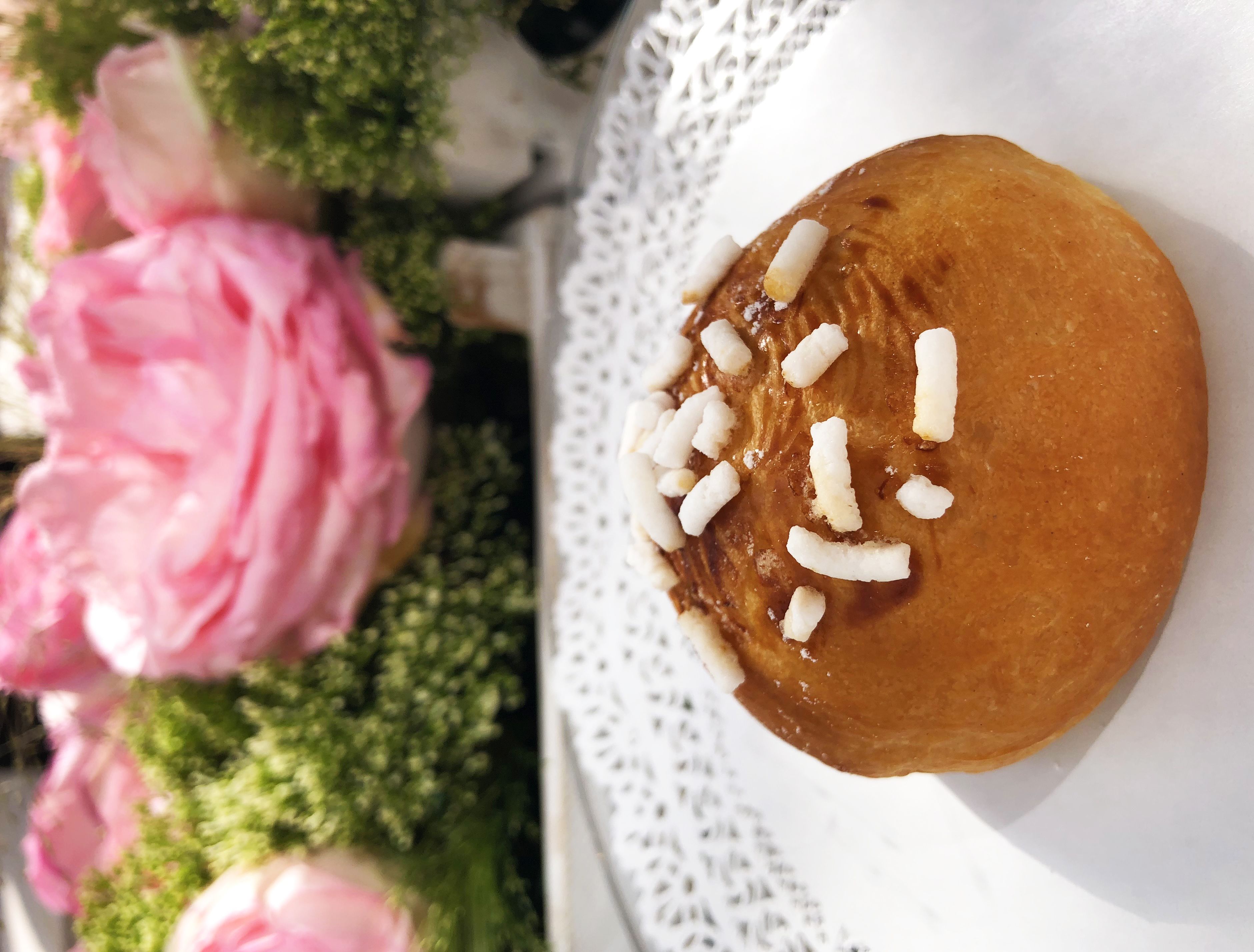 A round pastry with white toppings on a white plate, surrounded by pink flowers.