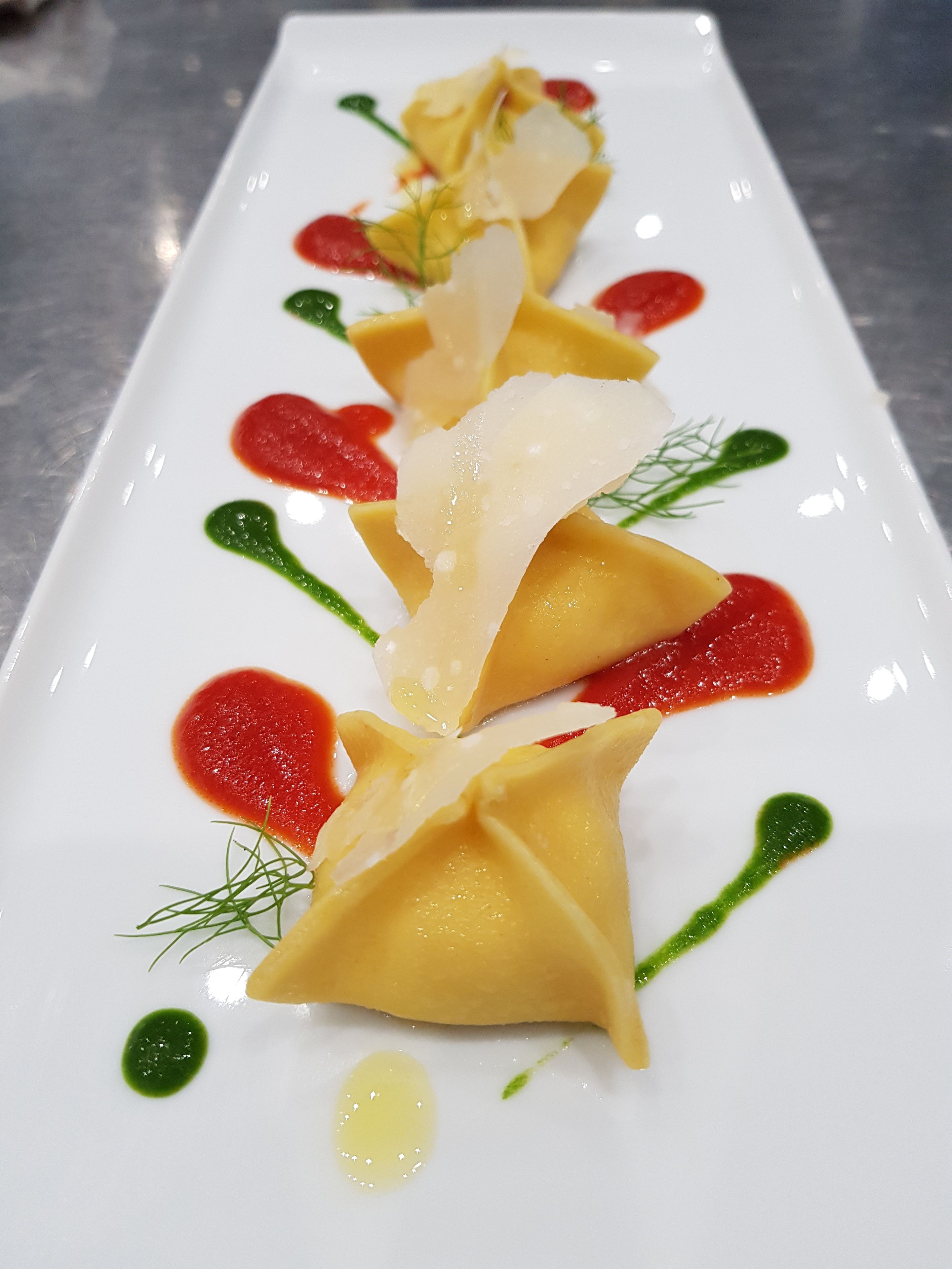 A rectangular white plate with a neatly arranged dish featuring pasta, garnishes, and sauces.