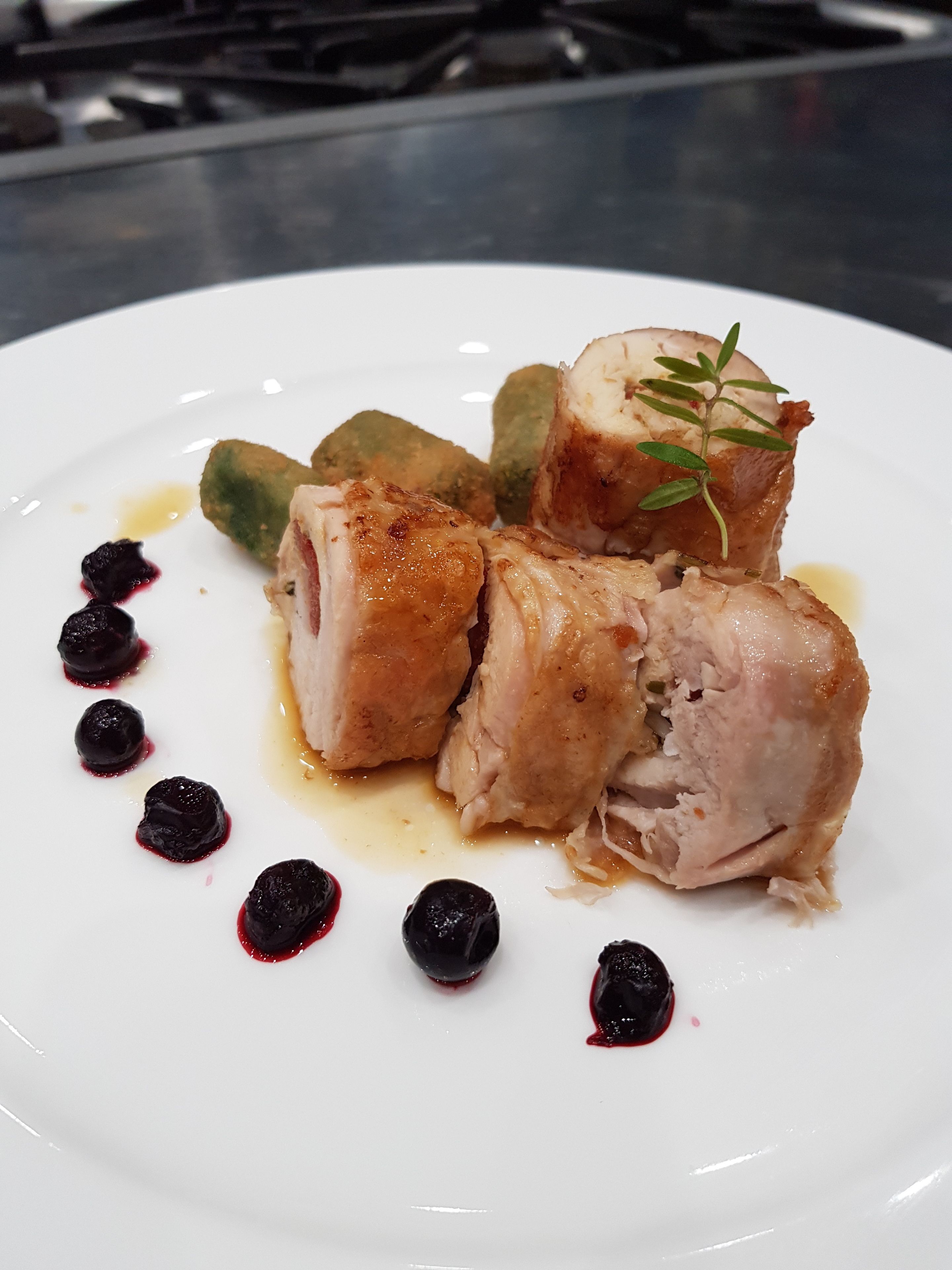 A white plate with a dish of meat, possibly pork, with a garnish of green leaves and a berry sauce.