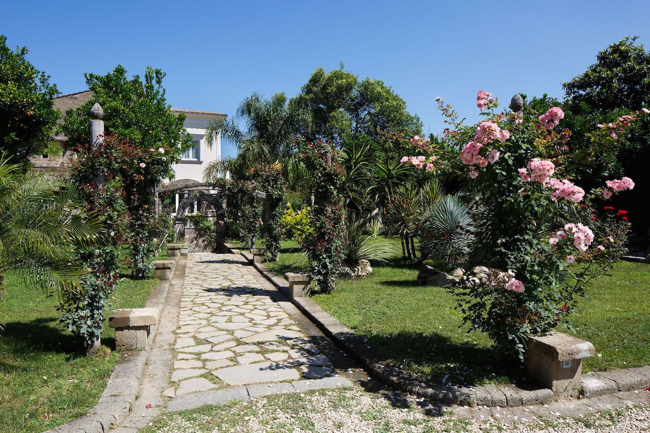A garden pathway leading to a building with a white facade and a tiled roof.