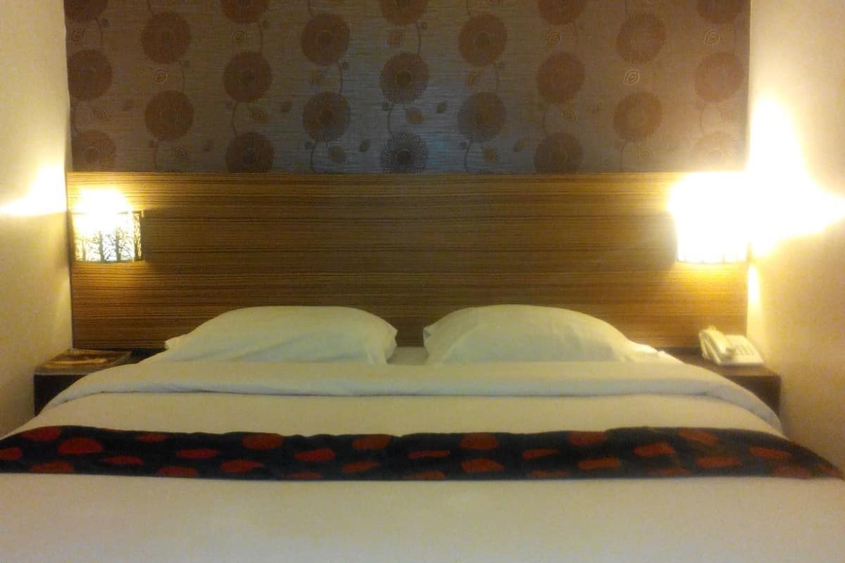 Ein Hotelzimmer mit einem hölzernen Kopfteil, zwei Nachttischlampen, einem Telefon und einem Bett mit weißer Bettwäsche.