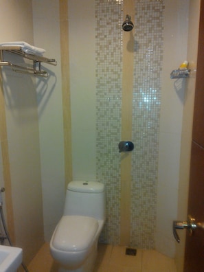 A small bathroom with a toilet, a shower with a tiled wall, and a towel rack. - Grand Hotel Lombok (Mataram)