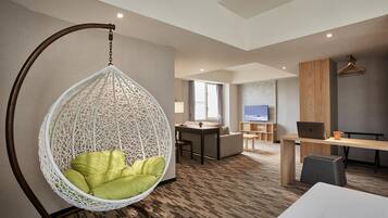A modern hotel room with a hanging chair, a desk with a laptop, a television, and a sofa.