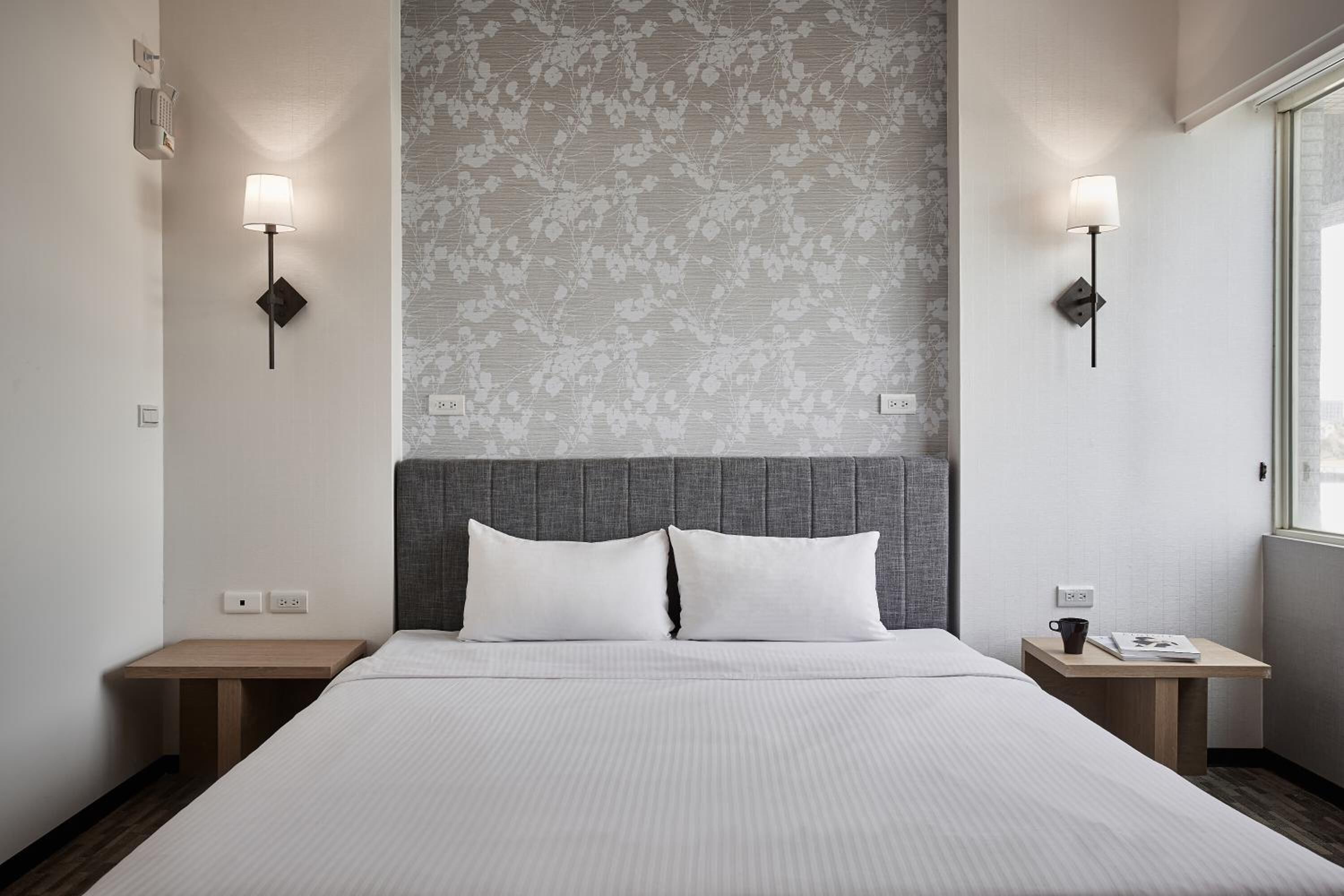 A hotel room with a large bed, two bedside tables, a wall-mounted lamp, and a patterned wallpaper.