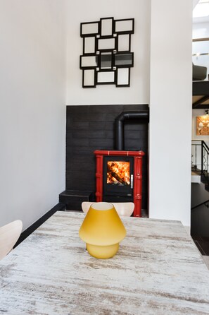 Una sala moderna con chimenea, una mesa con lámpara amarilla y una obra de arte geométrica en la pared.