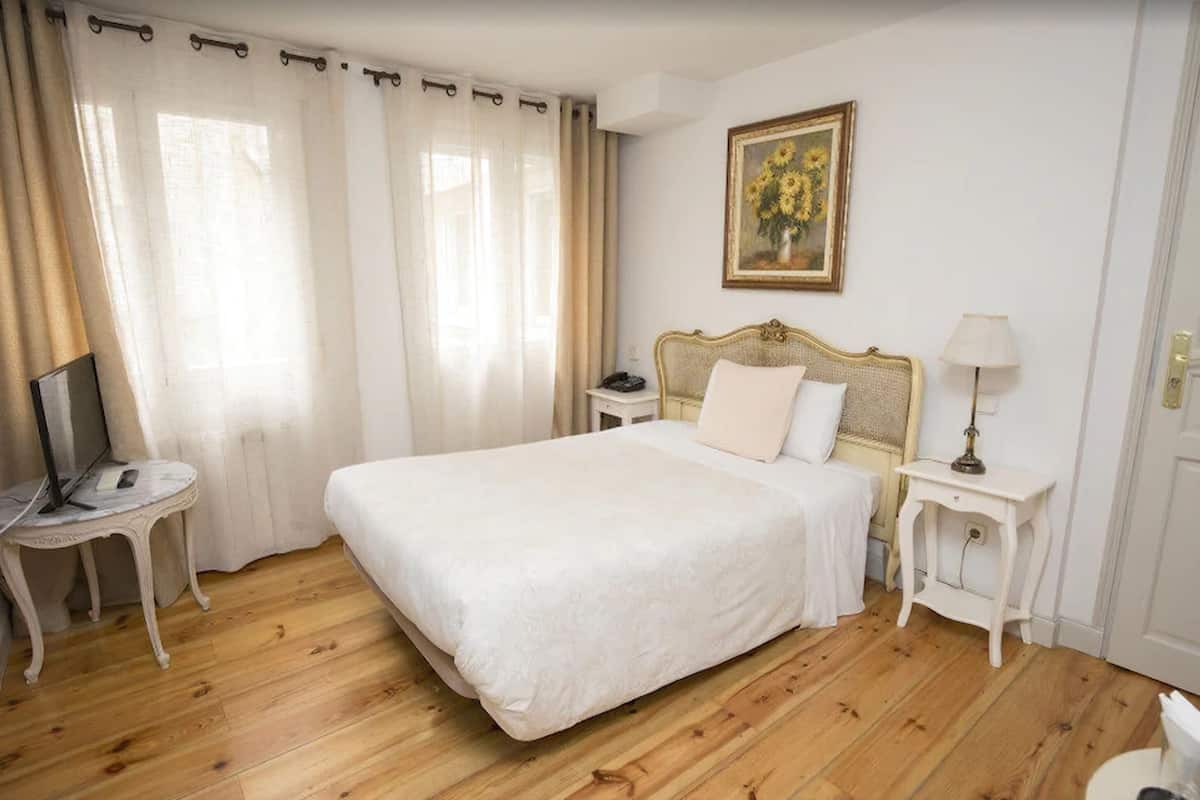 Un dormitorio ordenado con una cama grande, una mesita de noche con una lámpara, una pequeña mesa con un ordenador portátil y un cuadro en la pared.