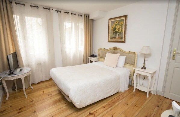 A neatly arranged bedroom with a large bed, a bedside table with a lamp, a small table with a laptop, and a painting on the wall. - Hostal Central Palace Madrid (Madrid)