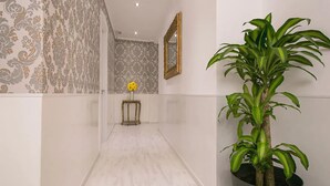 A hallway with patterned wallpaper, a potted plant, a small table with a vase of flowers, and a mirror on the wall. - Hostal Central Palace Madrid (Madrid)