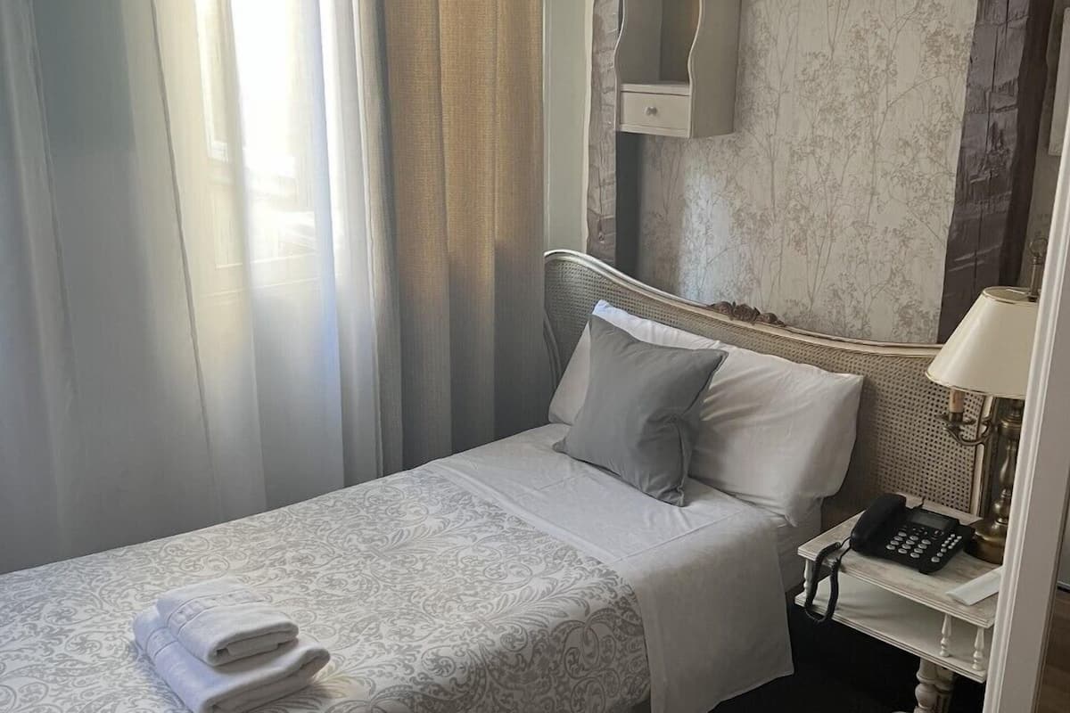 Una cama bien hecha con una colcha estampada y almohadas, un teléfono en la mesita de noche y un reloj de pared.