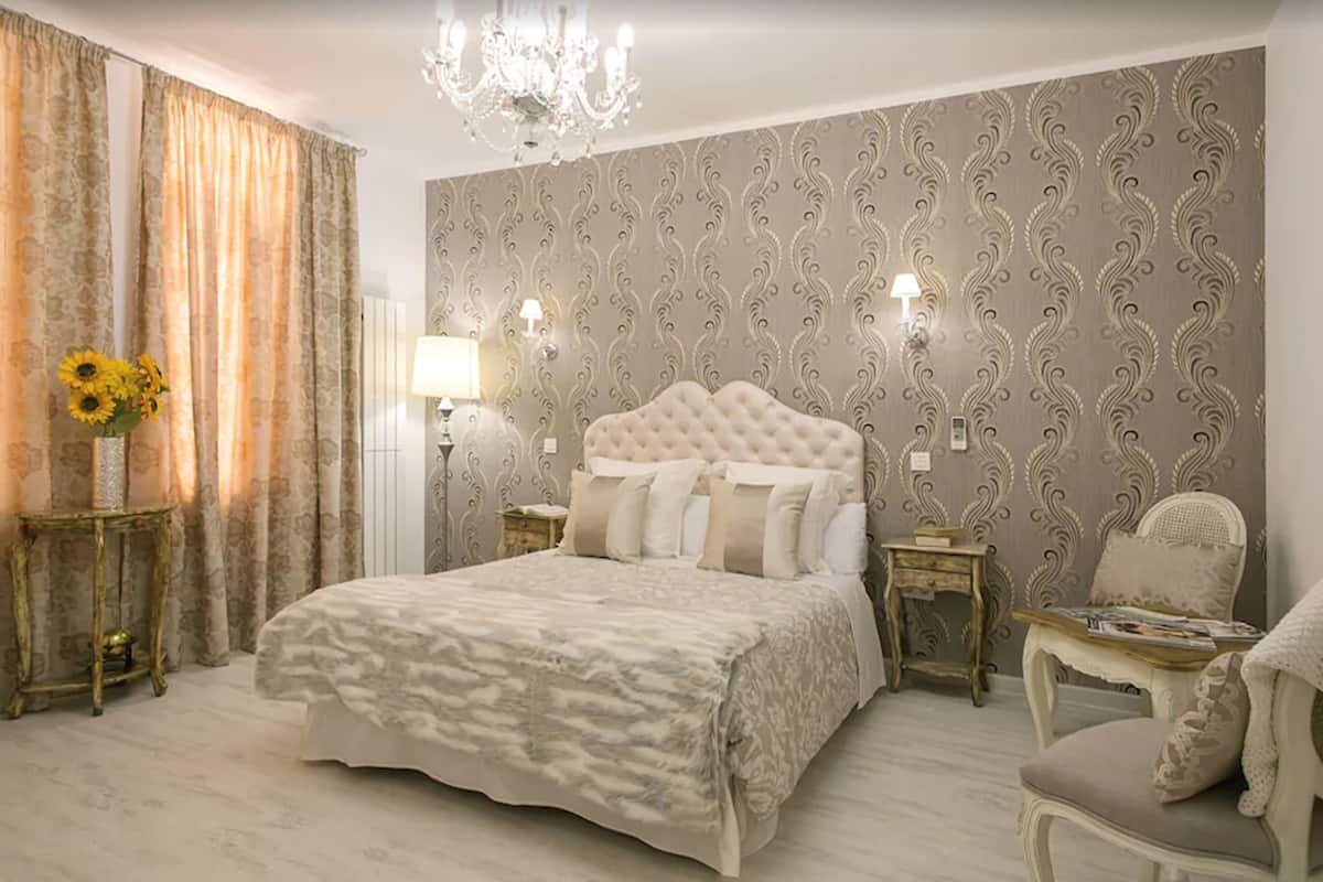 Un dormitorio con una cama grande, una araña, papel tapiz estampado y una mesita de noche con lámpara.