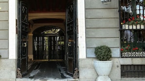 A building entrance with black double doors, a sign above the left door, and two potted plants on either side. - Hostal Central Palace Madrid (Madrid)