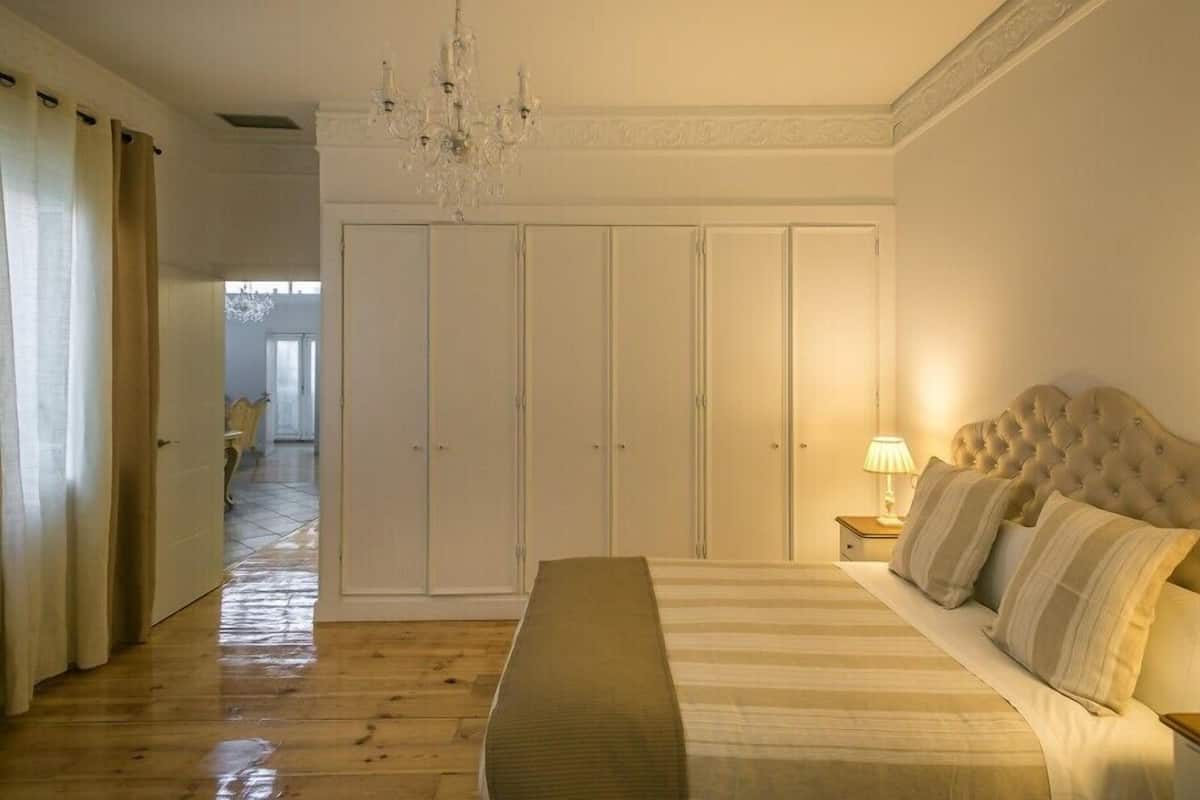 Un dormitorio con cama, banca, mesita de noche, candelabro y armario.