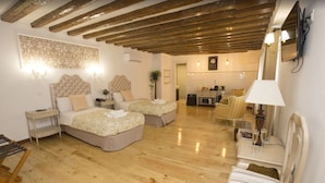 A spacious bedroom with two beds, a wooden floor, a dining area with a chair, and a kitchen in the background. - Hostal Central Palace Madrid (Madrid)