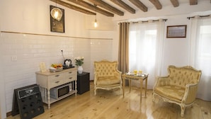A cozy room with a wooden floor, a white brick wall, a small table with a vase, two armchairs, and a white cabinet with a microwave. - Hostal Central Palace Madrid (Madrid)
