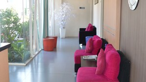 Un espace d’accueil d’hôtel avec un mur en verre, une plante en pot et deux canapés rouges.