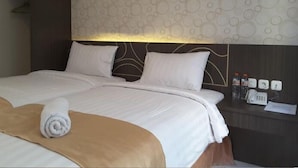 Une chambre d’hôtel avec un grand lit, deux oreillers, une table de chevet avec un téléphone et des bouteilles, et un mur décoré d’un motif.
