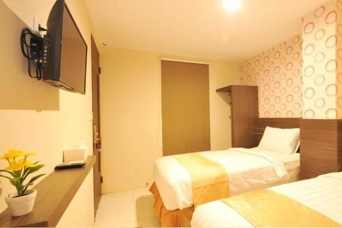 Habitación de hotel con dos camas, un televisor montado en la pared, una mesita con una planta y un papel tapiz decorativo.