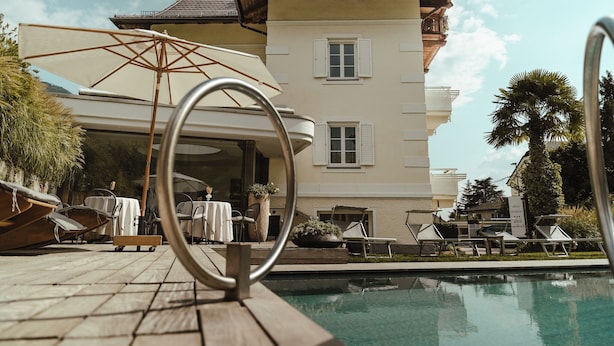 A poolside area with lounge chairs, a table, and a large umbrella. - Hotel Villa Freiheim (Merano)