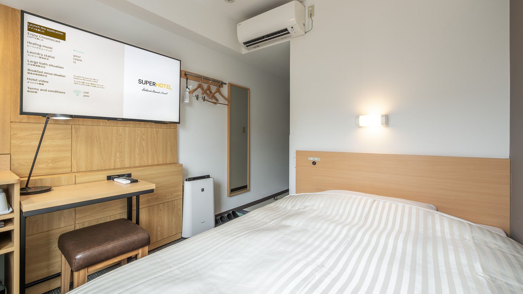 Habitació d'hotel amb llit, escriptori, cadira i televisió penjada a la paret que mostra un menú.
