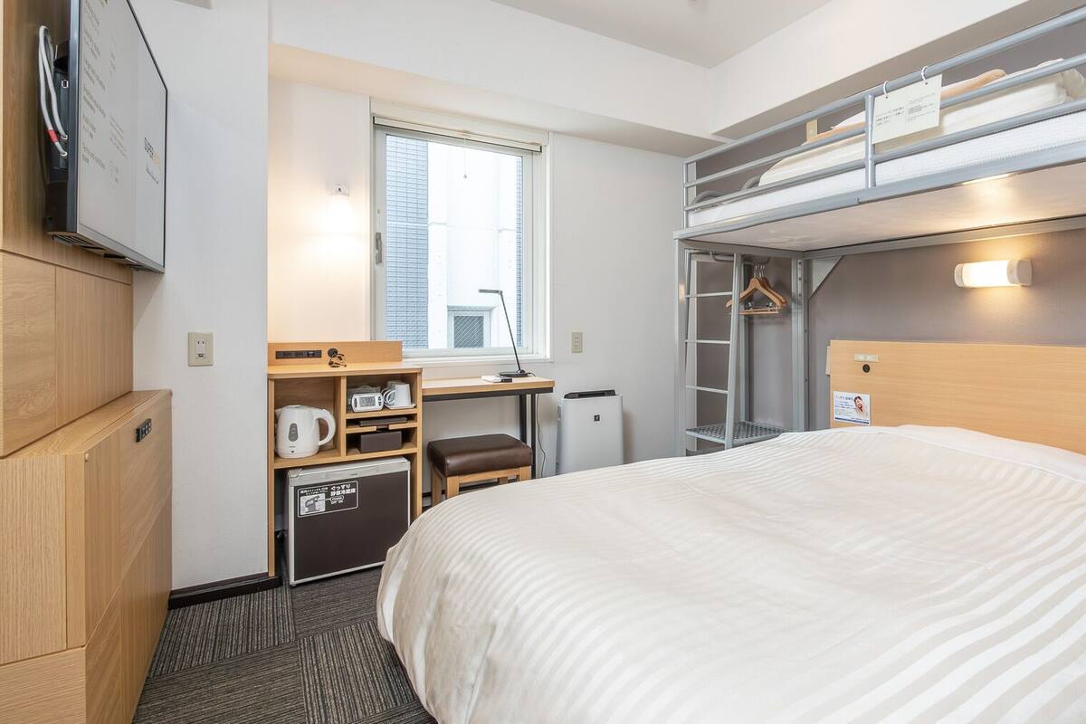 Ein Hotelzimmer mit Etagenbett, Schreibtisch mit Stuhl, einer kleinen Küchenzeile und einem Fenster.