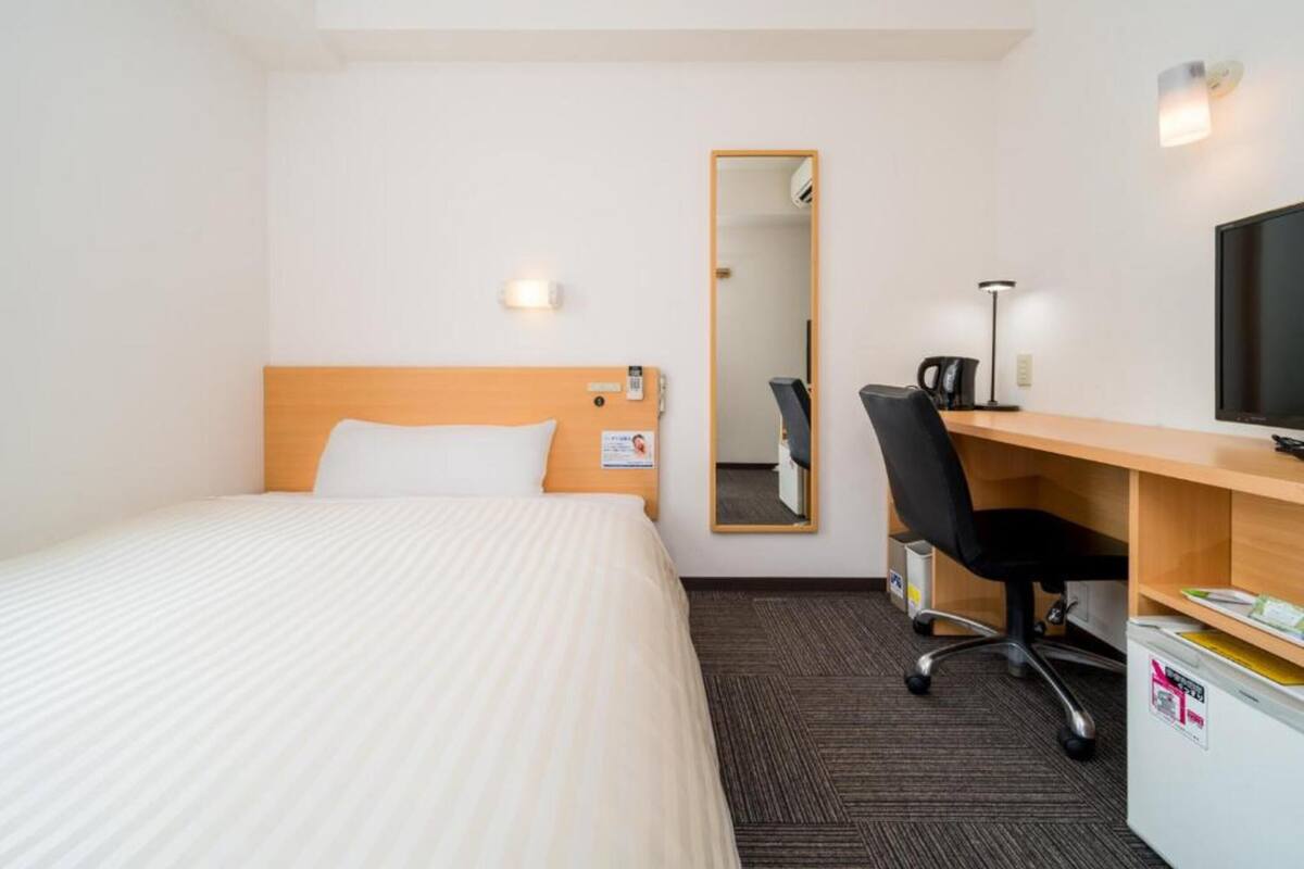 Ein Hotelzimmer mit einem Bett, einem Schreibtisch, einem Sessel, einem Fernseher und einem Spiegel.
