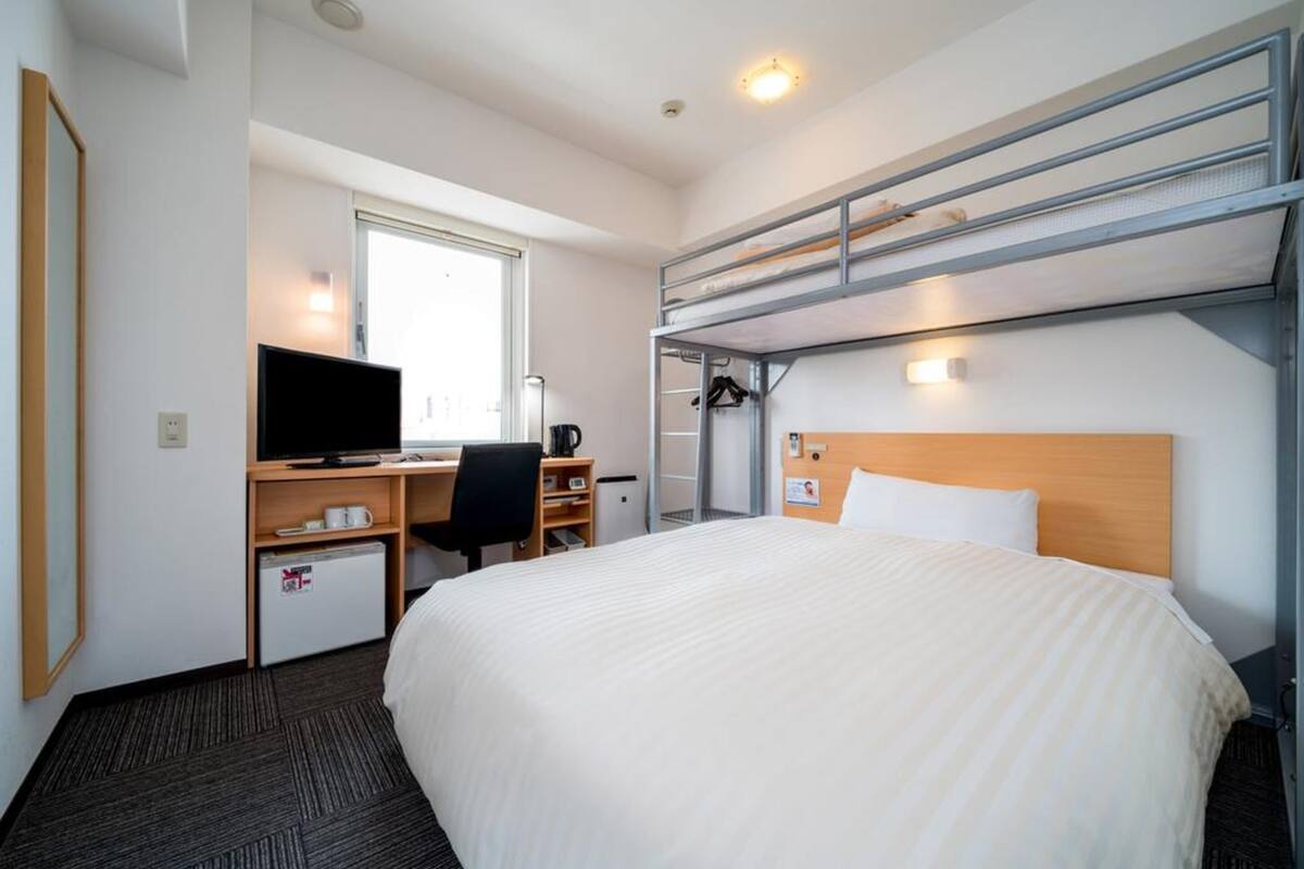 Ein Hotelzimmer mit einem Bett, einem Schreibtisch mit Computer, einem Fernseher und einem Fenster.