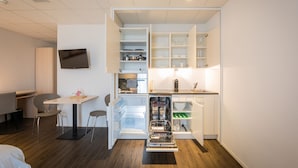 A compact hotel room with a kitchenette, a dining area with a table and chairs, and a flat-screen TV mounted on the wall.