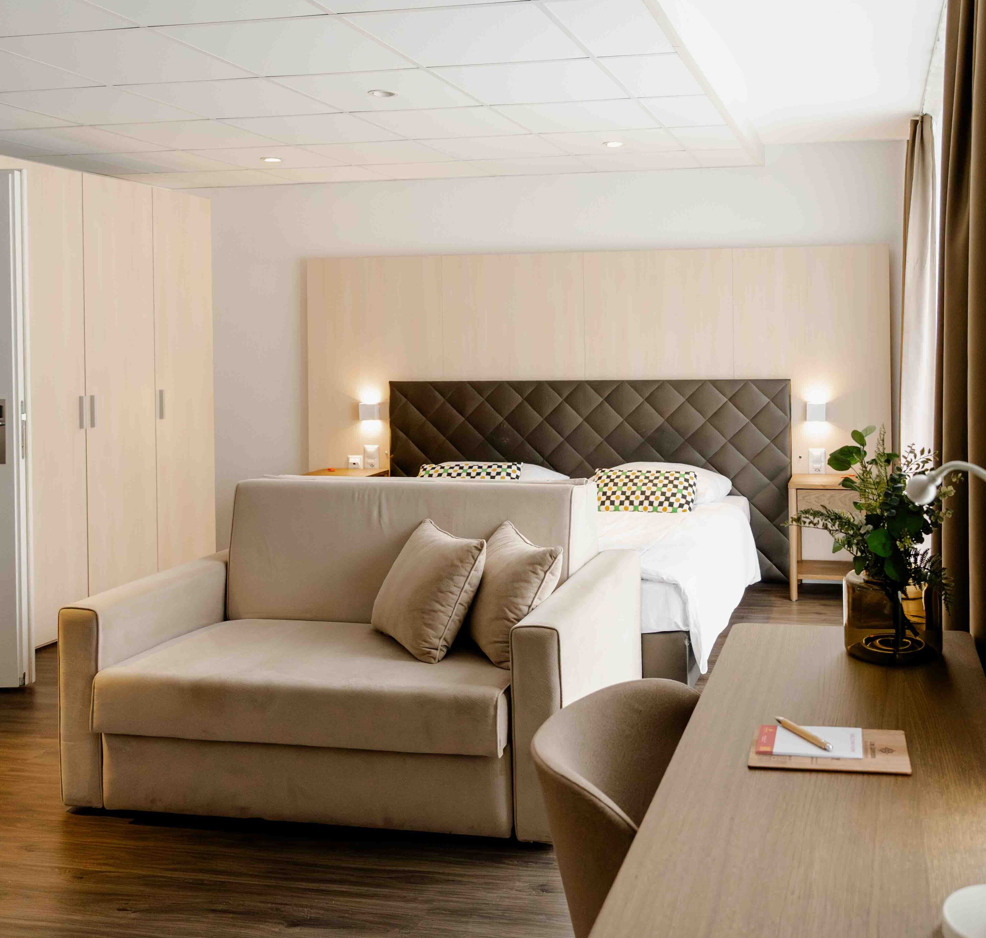 Una habitación de hotel con una cama, un sofá, un escritorio y una mesita de noche con lámpara.