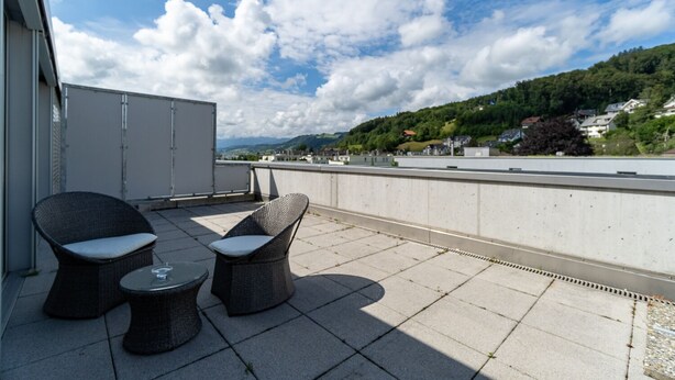 A rooftop terrace with wicker furniture and a clear view of a river and hills.